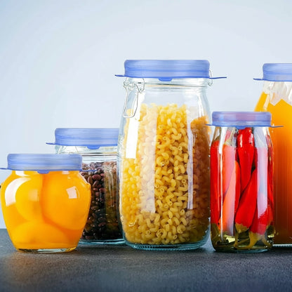 Essential Selects blue silicone stretch lids sealing various glass jars filled with food on a dark countertop.