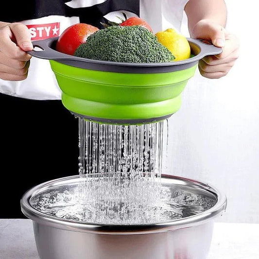 Essential Selects green collapsible silicone colander held over a metal bowl while rinsing fresh broccoli and fruit