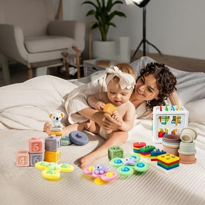 Essential Selects 6-in-1 Montessori baby toy set with colorful silicone blocks, stacking cups, and spinners on a bed.